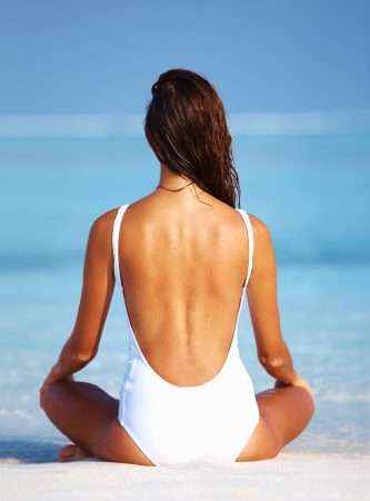 Rear view of young woman meditating in sexy swimwear on beach